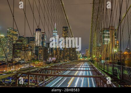 Vue sur le pont de Brooklyn avec la silhouette éclairée des gratte-ciel dans le centre de Manhattan pour une longue exposition de nuit Banque D'Images