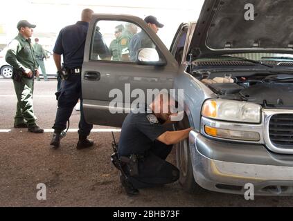 Laredo, Texas États-Unis, 14 juillet 2010: Des agents fédéraux, y compris la patrouille frontalière des États-Unis (vert), les douanes américaines (bleu) et les adjoints du shérif du comté de Webb inspectent les voitures en direction du Mexique au port d'entrée de Laredo, au Texas. Les agents sont à la recherche d'argent et de drogues qui se dirigent vers le Mexique à la suite de la violence accrue et du trafic de drogues le long de la frontière. ©Marjorie Kamys Cotera/Bob Daemmrich Photographie Banque D'Images