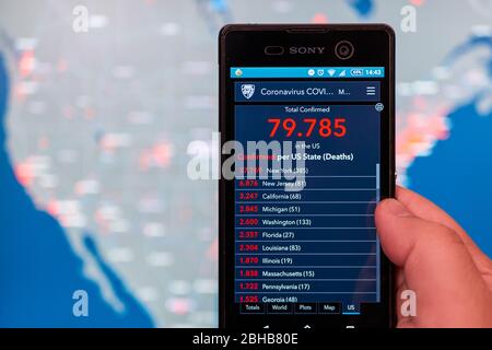 Man détient un smartphone avec Coronavirus COVID-19 mis à jour statistiques en direct des cas confirmés par le comté des États-Unis et carte des États-Unis en arrière-plan, Mexique, en mars 26, 2020 Banque D'Images