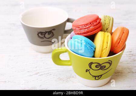 Délicieux macarons et tasses colorés sur fond en bois couleur Banque D'Images