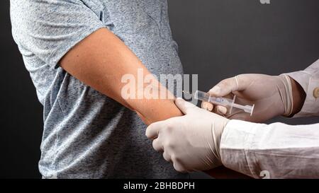 le médecin fait une injection dans le bras du patient sur un fond sombre. vaccination, médecine, traitement. Banque D'Images