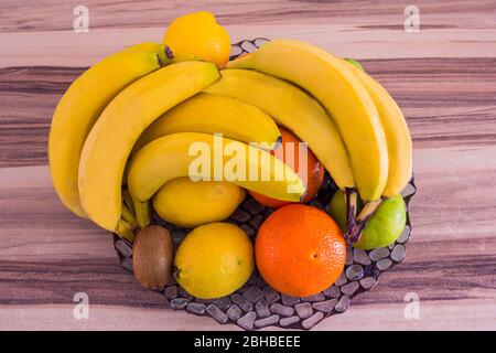 Vue de dessus d'un grand bol en verre plein d'oranges, de bananes, de citrons et d'autres fruits sur une table en bois Banque D'Images