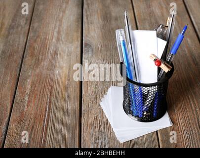 Différents stylos dans le support métallique avec notes en papier sur fond de planches en bois Banque D'Images