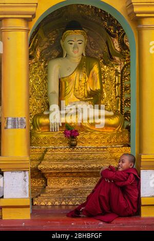 Jeune garçon se reposant devant les statues houlettes de la pagode Shwedagon à Yangon, au Myanmar Banque D'Images