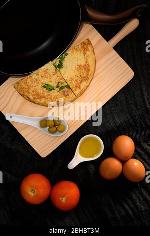 Une vue verticale de clôture à angle élevé de deux omelettes sur un bureau de cuisine en bois avec olives, jaune d'œuf, tomates et œufs frais sur les côtés Banque D'Images