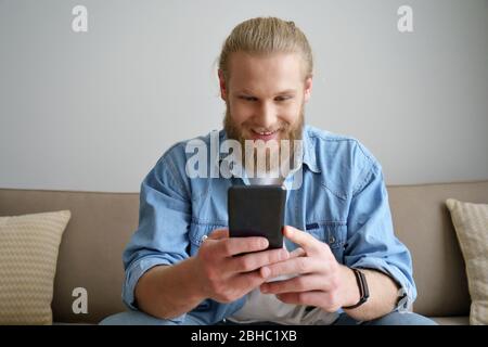 Un homme de technologie se reposant sur un canapé en utilisant un smartphone pour jouer à la maison. Banque D'Images