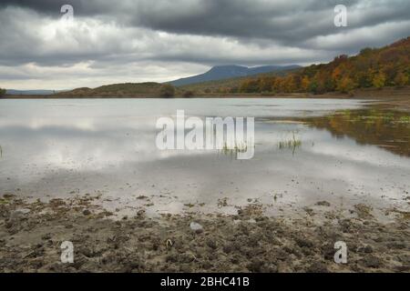 La pluie vient sur le lac parmi les montagnes vallonnées avec des arbres d'automne. Saleté et étang. Composition de la nature. Banque D'Images