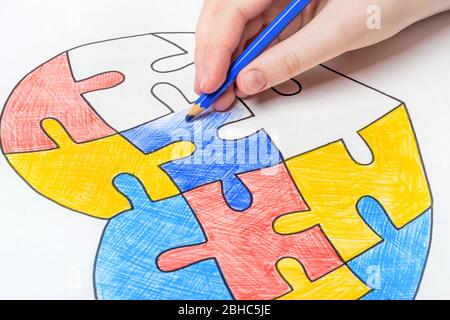 Journée mondiale de sensibilisation à l'autisme. La main des enfants tire le coeur des puzzles multicolores. Concept de soins de santé mentale. Banque D'Images