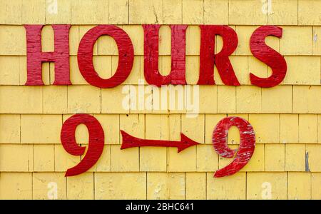 Affiche des heures de magasinage sur la façade de la boutique de cadeaux Seagull's Nest. Lettres peintes en rouge sur la parement de bardeaux peints en jaune. Port de North Rustico, Î.-P.-É., Canada Banque D'Images