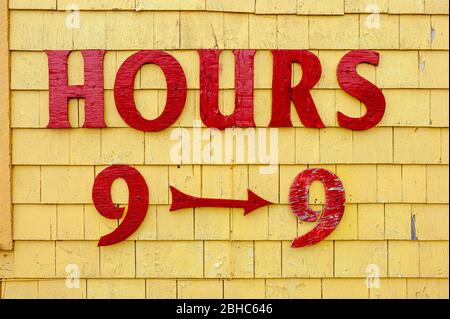 Affiche des heures de magasinage sur la façade de la boutique de cadeaux Seagull's Nest. Lettres peintes en rouge sur la parement de bardeaux peints en jaune. Port de North Rustico, Î.-P.-É., Canada Banque D'Images