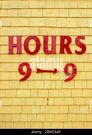 Affiche des heures de magasinage sur la façade de la boutique de cadeaux Seagull's Nest. Lettres peintes en rouge sur la parement de bardeaux peints en jaune. Port de North Rustico, Î.-P.-É., Canada Banque D'Images