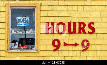 Les heures de magasinage sont affichées sur la façade de la boutique de cadeaux Seagull's Nest. Lettres rouges sur les bardeaux peints en jaune. Fenêtre avec panneau ouvert. North Rustico Harbour, Î.-P.-É., CA Banque D'Images