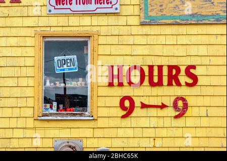 Les heures de magasinage sont affichées sur la façade de la boutique de cadeaux Seagull's Nest. Lettres rouges sur les bardeaux peints en jaune. Fenêtre avec panneau ouvert. North Rustico Harbour, Î.-P.-É., CA Banque D'Images