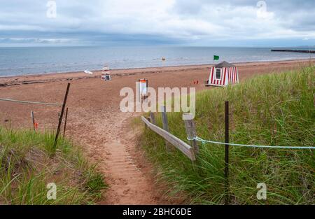 Chemin à travers les dunes de sable jusqu'à une plage déserte en bord de mer. Station de sauveteurs battant un drapeau vert signalant le surf calme. North Rustico Beach, Î.-P.-É., Canada Banque D'Images