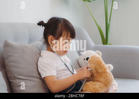 Soyez attentif. Agréable fille pensive occupée traitant l'ours en peluche assis sur le canapé Banque D'Images