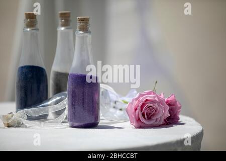 Trois bouteilles remplies de sable violet, bleu et vert sur une table décorée de ruban et de roses piink pour une cérémonie de mariage Banque D'Images