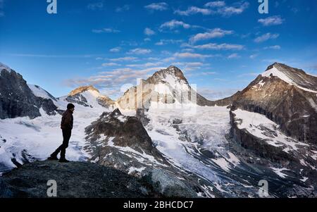 Randonneur d'homme accueillant une nouvelle journée dans les Alpes suisses, le soleil lumineux du matin brille aux sommets, dent Blanche, alors que la vallée est encore à l'ombre Banque D'Images