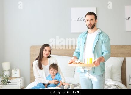 Un homme heureux qui a apporté son petit déjeuner familial au lit Banque D'Images