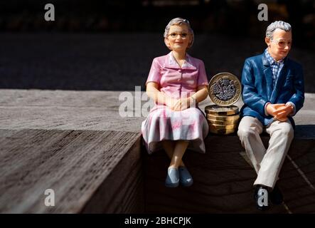 Couple de retraités, figurines miniatures, assis avec une livre de pièces, sur une surface en bois Banque D'Images