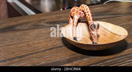 Petite girafe en bois tout en buvant sur une plaque en bois Banque D'Images