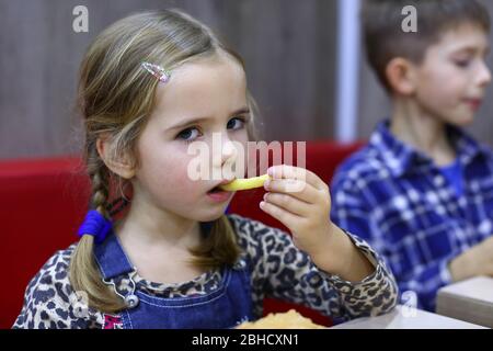 Portrait d'une jeune fille caucasienne de quatre ans qui mange des frites dans un café Banque D'Images