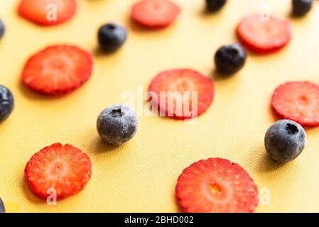 fraises et bleuets mûrs, frais et naturels coupés en rouge, un printemps sain et des fruits d'été, sur fond jaune Banque D'Images