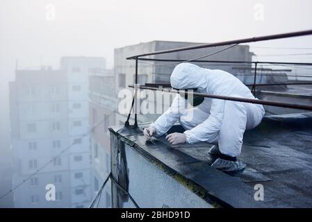 Scientifique collecte des échantillons par brucelles pour analyse dans la zone d'exclusion dangereuse, travaillant sur le toit du bâtiment haut, vue latérale, espace de copie Banque D'Images
