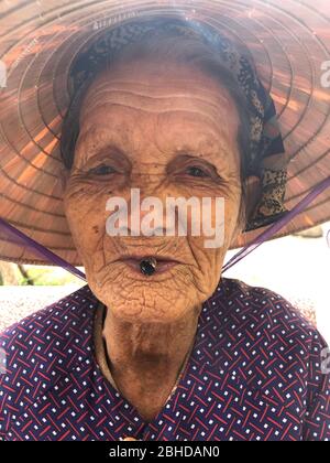 Hoi an, Vietnam, 20 janvier 2020 - vieille dame vietnamienne froissée fume et regardant l'appareil photo Banque D'Images