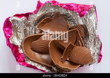 Chocolat au lait oeuf de Pâques cassé en morceaux dans une feuille d'argent rose isolée sur fond blanc Banque D'Images