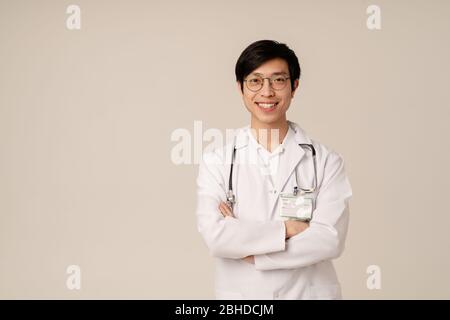 Image du jeune médecin asiatique en uniforme blanc médical, souriant isolé sur fond beige Banque D'Images