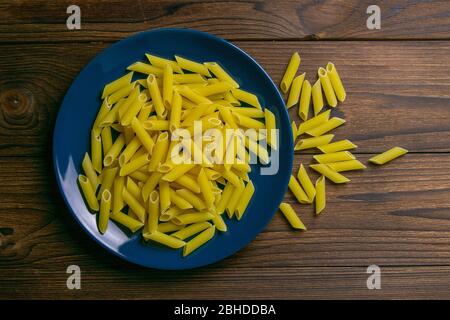 Penne Lisce pâtes en plaque bleue sur fond en bois sombre. Vues de dessus Banque D'Images