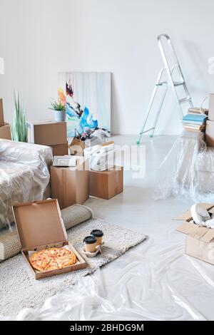 Boîte ouverte avec pizza appétissante livrée et deux verres de café au sol par canapé entouré de boîtes emballées et d'autres choses Banque D'Images