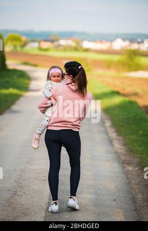 Mère et enfant marchant sur la route de campagne entre les champs agricoles vers le vilage de la forêt Banque D'Images