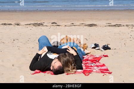 Portobello, Écosse, Royaume-Uni. 25 avril 2020. Vue sur les personnes en plein air le samedi après-midi sur la plage et la promenade de Portobello, à Édimbourg. Le beau temps a amené plus de gens à faire de la marche et du vélo à l'extérieur. La police patrouillait dans les véhicules mais ne s'arrête pas parce que la plupart des gens semblent observer des distances sociales. Couple se couchant sur la plage. Iain Masterton/Alay Live News Banque D'Images