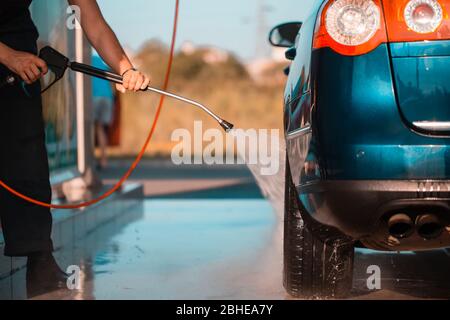 Un travailleur masculin qui se lave la voiture sous l'eau haute pression à l'extérieur Banque D'Images