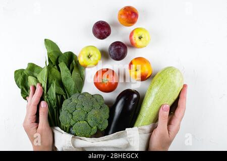 Mains féminines tenant des légumes végétaliens dans un sac réutilisable en cotons sur une table légère. Zéro déchet, soins, concept de santé. Vue de dessus, espace de copie, plat. Banque D'Images