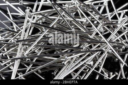 pile de broches à coudre droites à tête plate disposées de manière aléatoire sur fond noir. Utilisé pour maintenir le tissu ensemble avant la couture Banque D'Images