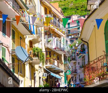 Manarola, Italie, 12 septembre 2018: Bâtiments colorés maisons avec drapeaux rangées, balcons, fenêtres de volets sur une rue étroite du village traditionnel typique de pêche Parc National Cinque Terre, Ligurie Banque D'Images