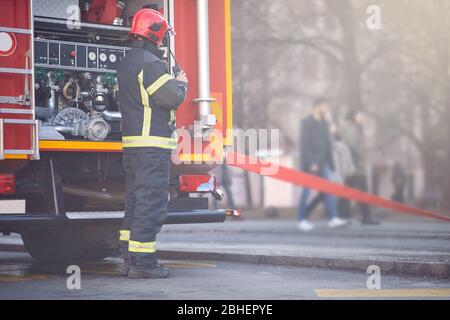 Travail des pompiers. Pompier avec uniforme et casque près d'un camion de pompiers. Banque D'Images