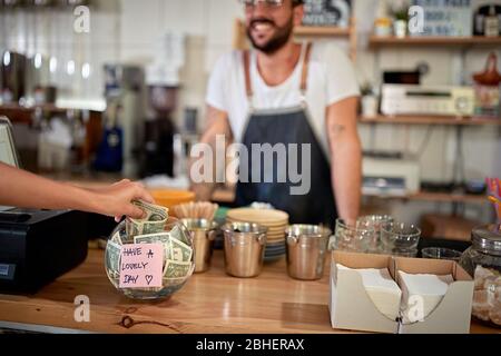 client satisfait dans un café-restaurant laissant un pourboire dans un bol avec un message positif sur un autocollant. argent, pourboire, satisfait, message positif Banque D'Images