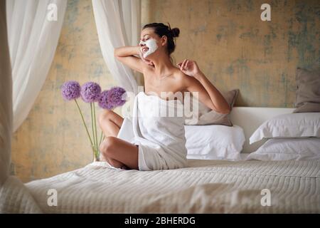 Jeune femme avec masque facial le matin au lit en appréciant et s'étirant Banque D'Images