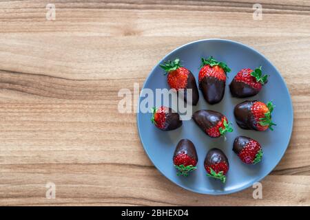 Vue de dessus des fraises fraîches et saines trempées dans du chocolat noir sur une plaque bleue avec un fond en bois Banque D'Images