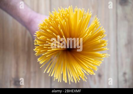 Les spaghettis non cuits, en rangée, sont rassemblés à la main. Pâtes italiennes ou macaroni. Œil d'oiseau, vue de dessus, fond de table en bois. Pâtes alimentaires sèches. Banque D'Images