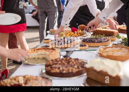 buffet de gâteaux avec des serveurs servant et des personnes esestivées prenant leurs parties à l'extérieur Banque D'Images