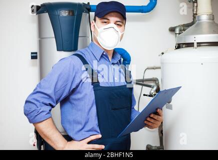 Technicien souriant qui s'est rendu sur un chauffe-eau pendant une pandémie de coronavirus Banque D'Images