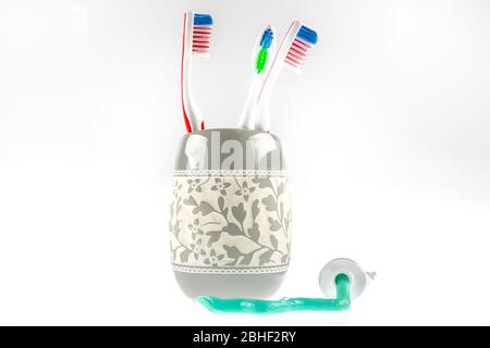 Le dentifrice vert et les brosses à dents multicolores se trouvent dans un verre spécial à côté d'un tube de dentifrice. Toujours la vie. Banque D'Images