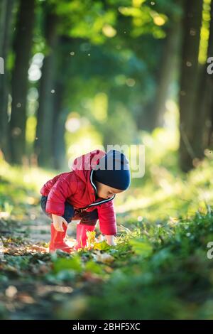 Petit garçon en caoutchouc rouge et veste rouge dans le parc de printemps. Feuilles de forêt verte luxuriante sur fond Banque D'Images
