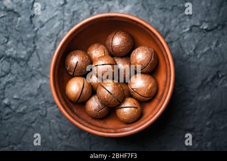 Noix de macadamia séchées dans un bol en céramique orange. Prise de vue macro studio. Fond en béton noir Banque D'Images