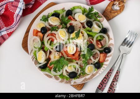 Salade saine avec thon en conserve, tomates, œufs de caille, olives noires, oignons blancs et laitue biologique sur fond blanc, vue de dessus, gros plan Banque D'Images