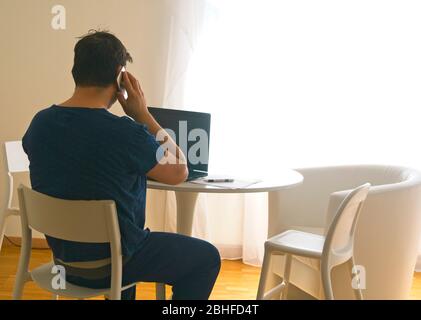 Jeune homme assis et travaillant sur un ordinateur portable à la maison parlant au mobile. Concept de père de travail. Concept de télétravail Banque D'Images